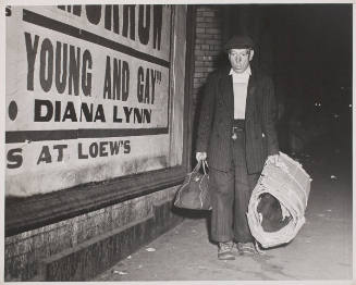 Untitled  (man in suit with bedroll walking beside poster)